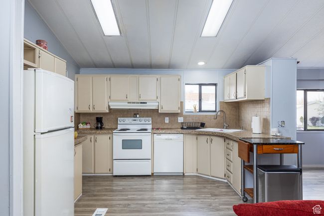 Kitchen featuring tasteful backsplash, white appliances, light wood-style flooring, under cabinet range hood, and a sink | Image 6