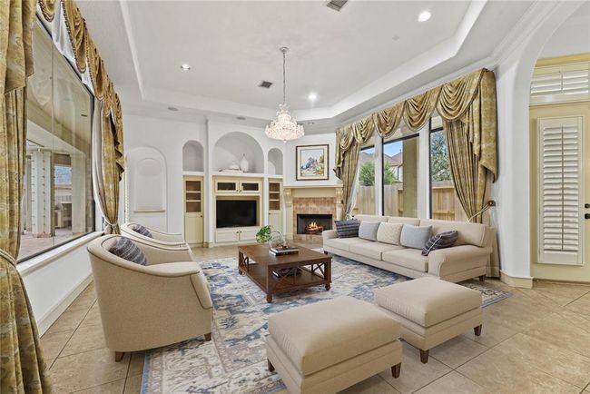 Grand living room showcases a magnificent chandelier, luxurious drapes, tiled flooring, media built-ins & a gas log fireplace—all overlooking your stunning pool oasis. Virtually staged to inspire your personal design vision. | Image 6