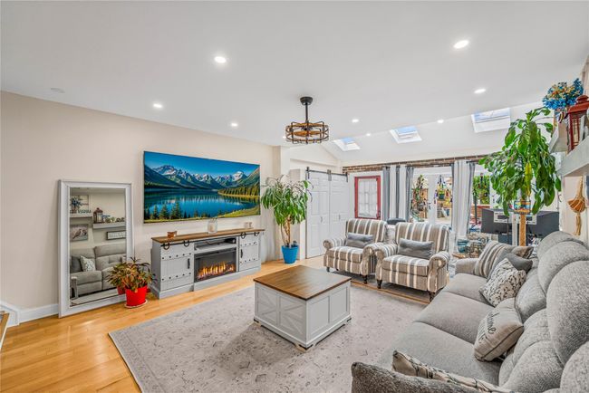 Living room with a glass covered fireplace, recessed lighting, light wood-style flooring, baseboards, and a skylight | Image 4
