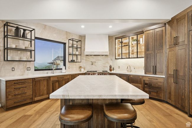 Kitchen featuring premium range hood, tasteful backsplash, light countertops, a center island, and light wood-type flooring | Image 25