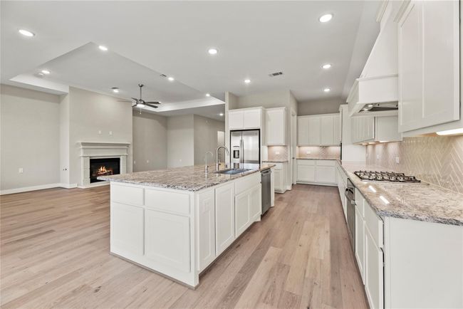 Show off your culinary skills in this fully loaded kitchen, where an oversized island with a deep basin sink and bar seating creates the perfect space for prep and gathering. Granite countertops, stainless steel appliances, herringbone tile backsplash, a walk-in pantry, and extensive cabinetry combine style and function for both daily meals and effortless entertaining. | Image 15