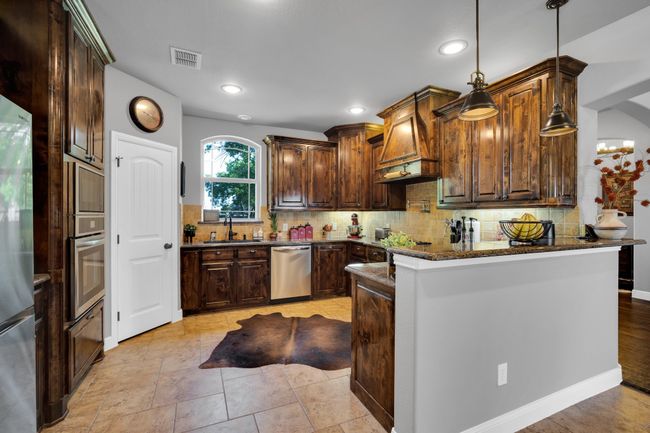 Kitchen featuring dark brown cabinets, appliances with stainless steel finishes, backsplash, dark stone counters, and light hardwood / wood-style flooring | Image 11
