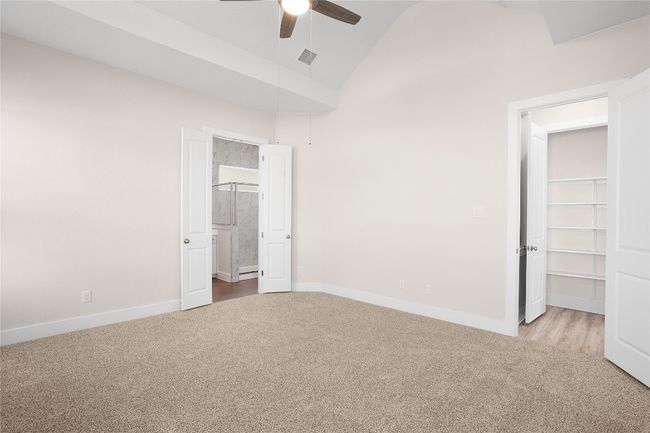 Unfurnished bedroom with carpet flooring, baseboards, ensuite bath, high vaulted ceiling, and a ceiling fan | Image 13