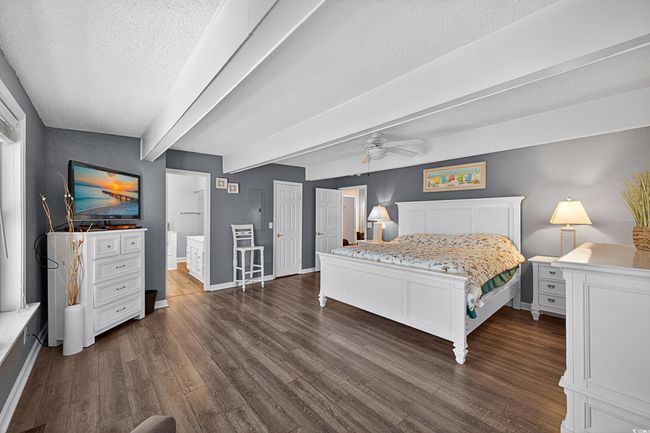 Bedroom featuring a textured ceiling, dark wood-style floors, beamed ceiling, ensuite bath, and a ceiling fan | Image 20