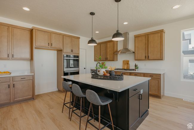Kitchen featuring baseboards, wall chimney range hood, light wood-style flooring, light countertops, and a kitchen island | Image 8