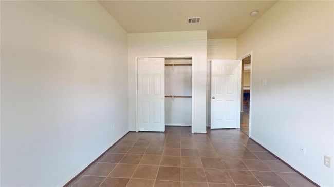 This room features neutral walls and tiled flooring, with a double-door closet and an adjacent door leading to another space. It's bright and versatile, ideal for a bedroom or office. | Image 7