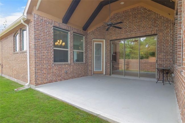 This photo showcases a covered patio with a brick exterior, featuring a ceiling fan and a concrete floor. Large sliding glass doors open to the interior, providing a spacious and inviting outdoor living area. | Image 40