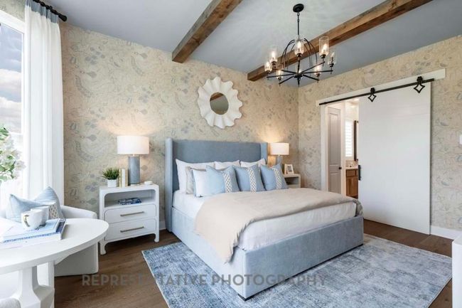 Bedroom featuring a barn door, beamed ceiling, wood finished floors, a chandelier, and wallpapered walls | Image 12