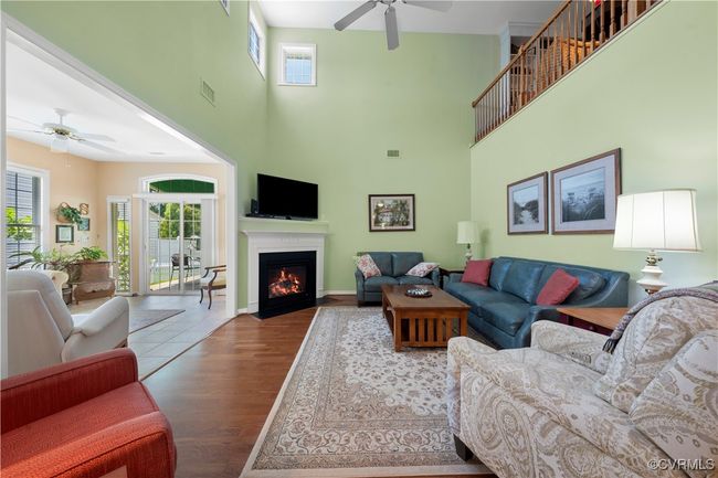 Living room featuring ceiling fan, a high ceiling, wood finished floors, and a fireplace with flush hearth | Image 12