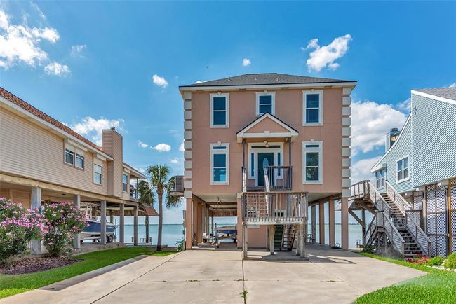 This elevated home features a spacious concrete drive, landscaped yard, and a covered ground-level area with walk-around access. The front entrance includes a set of stairs that leads to a covered entry before entering the main floor. | Image 43