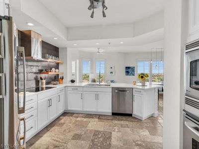 Kitchen featuring white cabinetry, appliances with stainless steel finishes, kitchen peninsula, ceiling fan, and light tile floors | Image 2