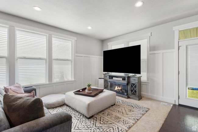 Living area with a decorative wall, wainscoting, wood finished floors, a glass covered fireplace, and recessed lighting | Image 6