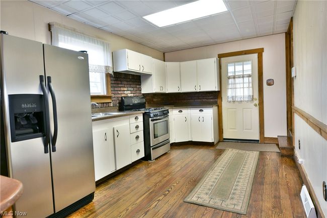 Kitchen with a drop ceiling, appliances with stainless steel finishes, tasteful backsplash, dark hardwood / wood-style flooring, and white cabinets | Image 8