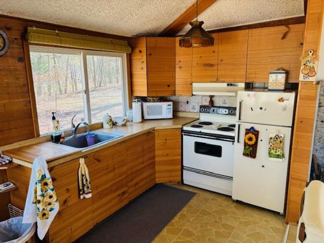 Kitchen with white appliances, sink, wooden walls, a textured ceiling, and decorative light fixtures | Image 9