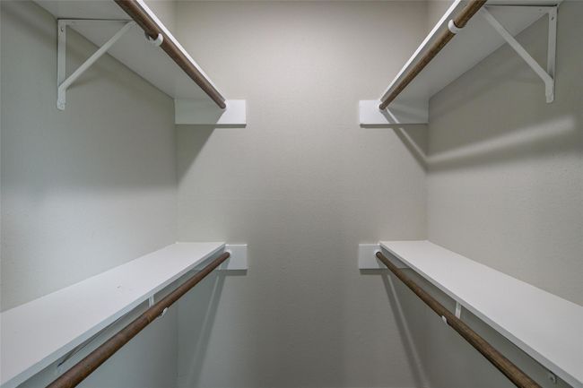 This photo shows a walk-in closet with multiple wooden rods and white shelves, providing ample storage space. | Image 18