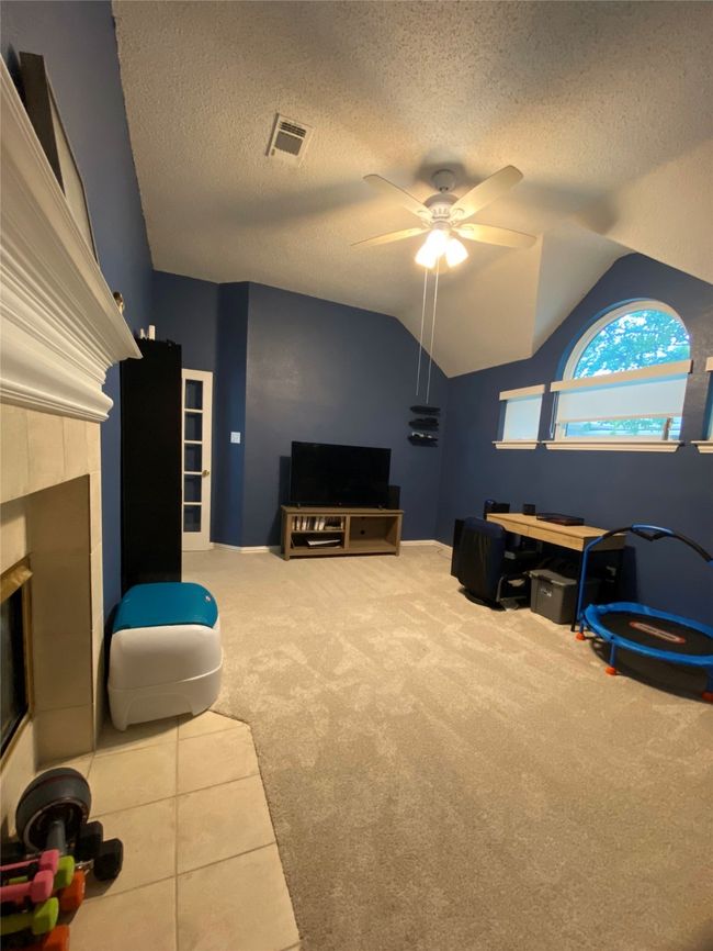 Carpeted living area with lofted ceiling, a textured ceiling, visible vents, a fireplace, and a ceiling fan | Image 17