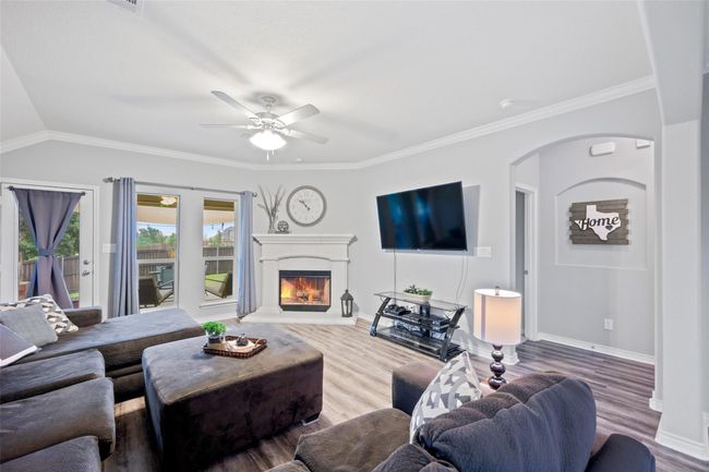 Living room featuring wood finished floors, a warm lit fireplace, a ceiling fan, baseboards, and arched walkways | Image 16