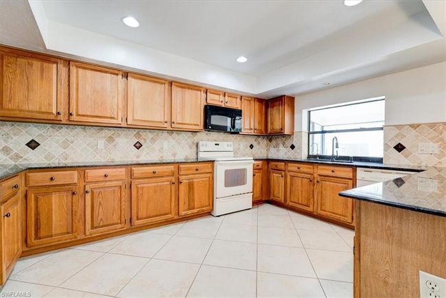Kitchen featuring dark stone counters, a tray ceiling, a sink, and white appliances | Image 15