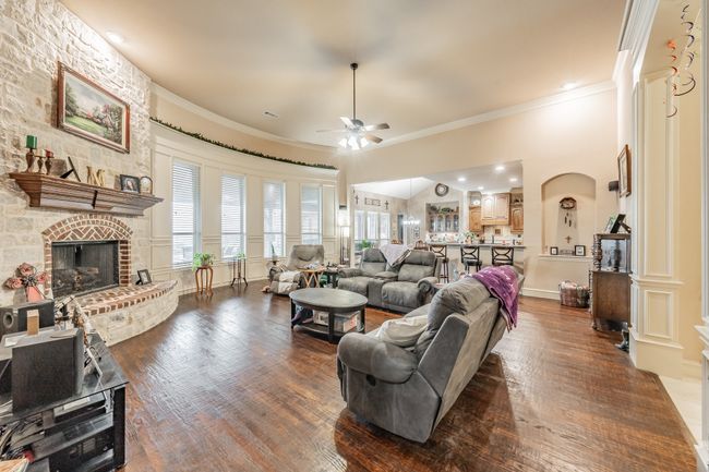 Living area featuring ceiling fan, ornamental molding, arched walkways, dark wood-style floors, and a brick fireplace | Image 5