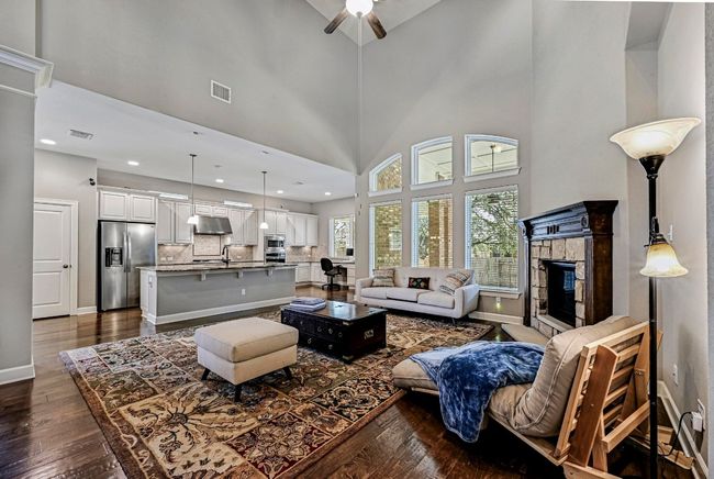 Living area with ceiling fan, dark wood-type flooring, a fireplace, and a towering ceiling | Image 5