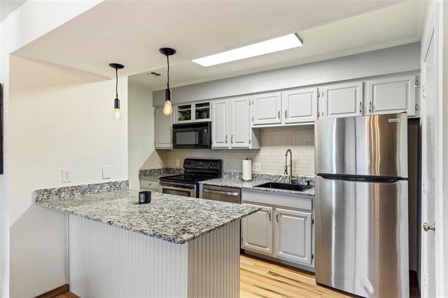 Kitchen featuring stainless steel appliances, a peninsula, light wood finished floors, backsplash, and light stone counters | Image 11
