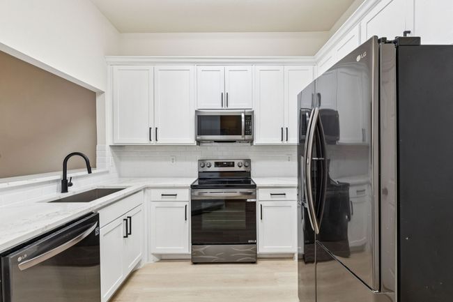 Kitchen with appliances with stainless steel finishes, light stone counters, white cabinetry, and decorative backsplash | Image 5