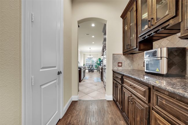 Kitchen with dark stone countertops, dark brown cabinetry, arched walkways, dark wood-style floors, and backsplash | Image 9