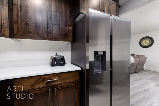 Kitchen featuring dark brown cabinetry, stainless steel refrigerator with ice dispenser, light countertops, light wood finished floors, and baseboards | Image 15