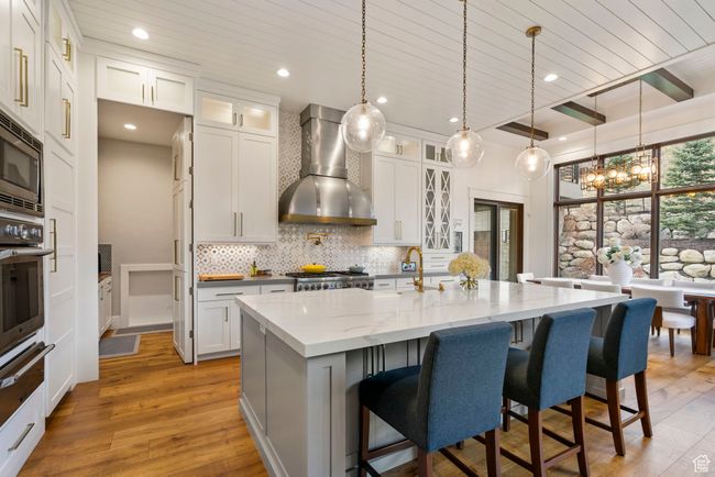 Kitchen featuring tasteful backsplash, hanging light fixtures, wall chimney exhaust hood, light wood-type flooring, and appliances with stainless steel finishes | Image 25