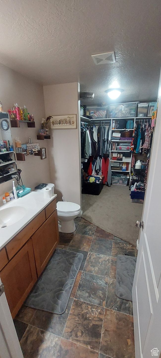 Bathroom with vanity, a textured ceiling, a walk in closet, and stone tile floors | Image 7