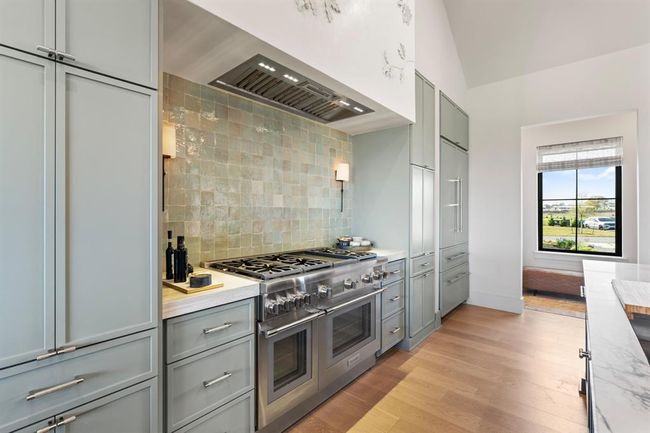 The kitchen features truly top-of-the-line Thermador appliances and Kohler plumbing fixtures. Custom solid wood cabinetry offers ample storage in a modern thin-shaker door styling. Decorative Zelige tile and sconces add dimension to the range's backsplash. | Image 11