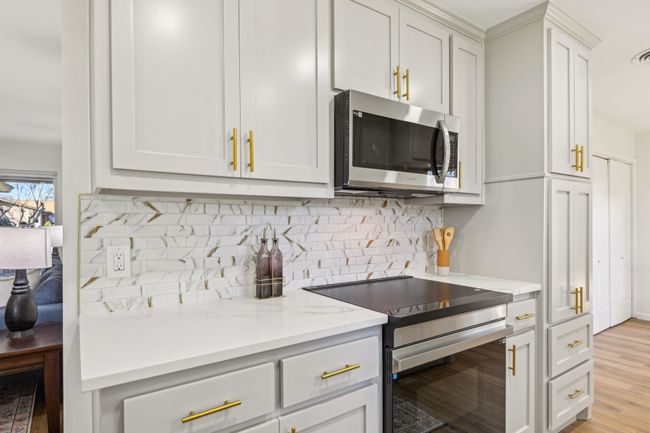 Kitchen with stainless steel microwave, electric stove, tasteful backsplash, light wood-style floors, and light stone countertops | Image 9
