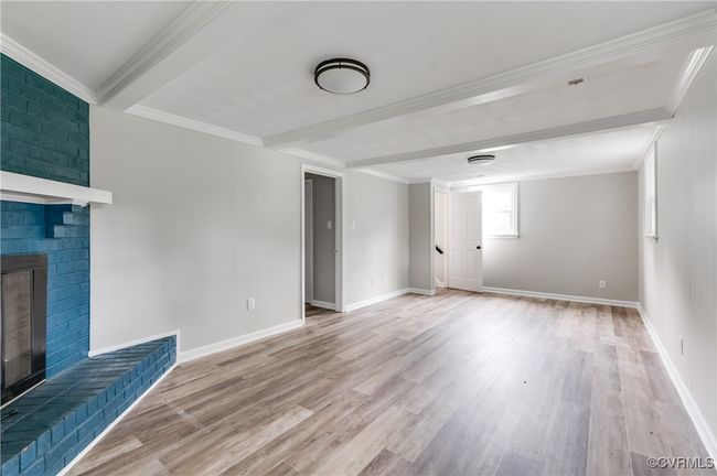 Unfurnished living room with beamed ceiling, light wood finished floors, crown molding, and a brick fireplace | Image 18