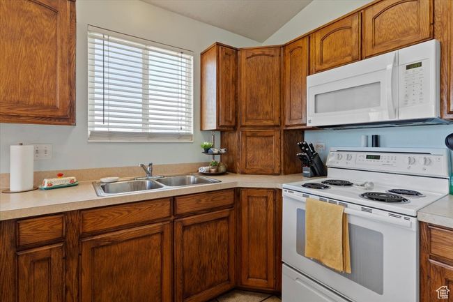 Kitchen with white appliances, a peninsula, a chandelier, vaulted ceiling, and light countertops | Image 11