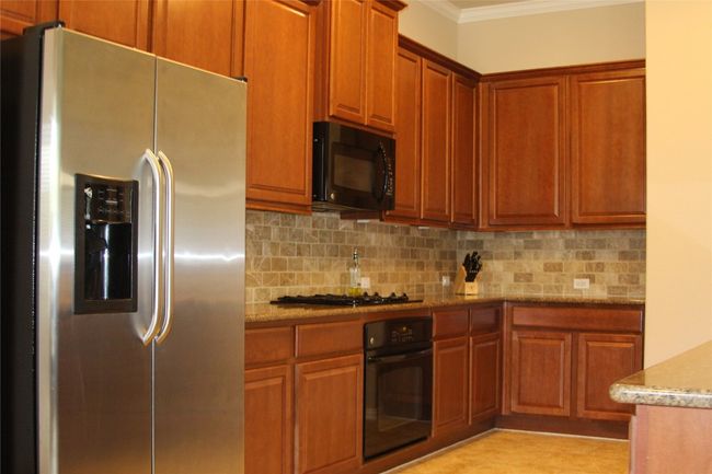 Kitchen featuring appliances, crown molding, backsplash, light stone countertops, and brown cabinets | Image 4