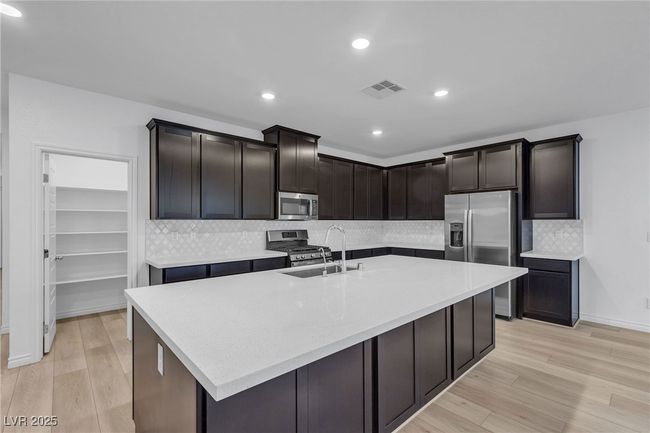 Kitchen featuring stainless steel appliances, a sink, light wood finished floors, tasteful backsplash, and a large island with sink | Image 6