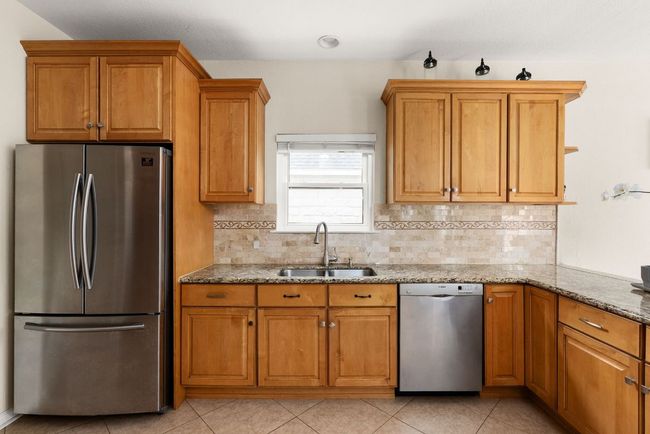 Kitchen with brown cabinetry, appliances with stainless steel finishes, a sink, and light stone counters | Image 9