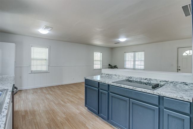 Kitchen with black electric cooktop, light wood-style flooring, blue cabinetry, wainscoting, and light stone counters | Image 13