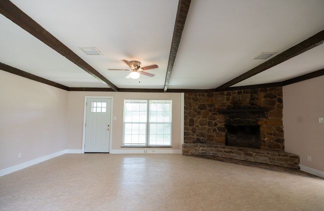 Unfurnished living room featuring beamed ceiling, a ceiling fan, and a stone fireplace | Image 8
