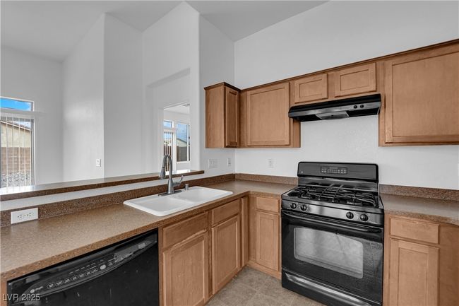 Kitchen with dark countertops, a sink, under cabinet range hood, and black appliances | Image 8