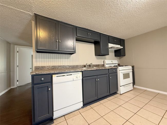 Kitchen featuring a textured ceiling, white appliances, baseboards, under cabinet range hood, and a sink | Image 7