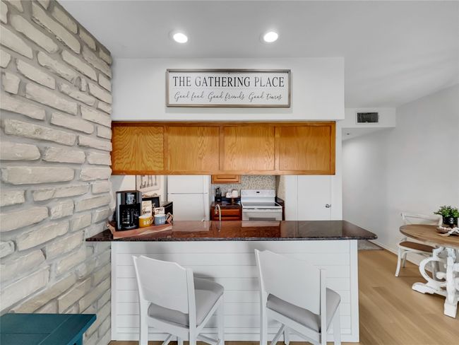 Kitchen featuring white appliances, a peninsula, a kitchen bar, light wood-style floors, and dark stone counters | Image 11