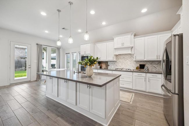 The gourmet kitchen features an expansive dine-in island adorned with custom pendant lighting, seamlessly flowing to convenient outdoor access, effortlessly combining refined style and exceptional functionality for every culinary experience. | Image 11