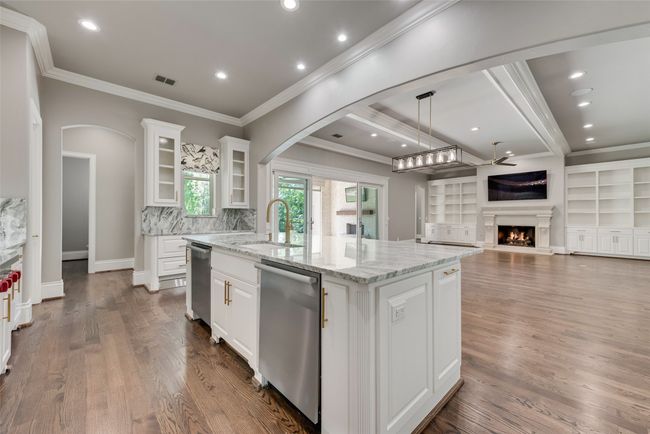 Kitchen with a kitchen island with sink, stainless steel dishwasher, arched walkways, a sink, and a warm lit fireplace | Image 13