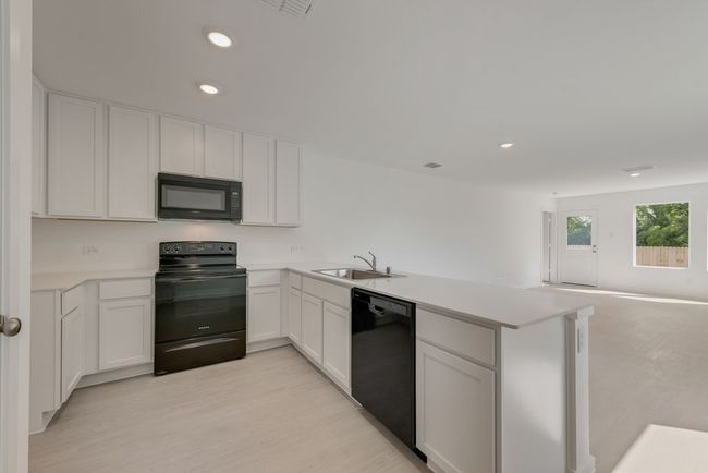 Kitchen with black appliances, light countertops, open floor plan, a peninsula, and white cabinets | Image 12