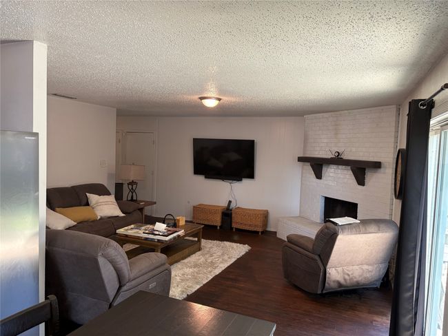 Living area with a textured ceiling, dark wood-type flooring, and a brick fireplace | Image 4