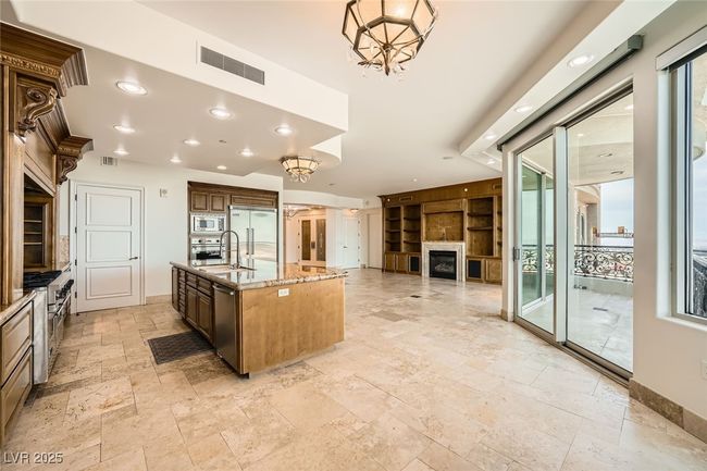Kitchen with stone tile flooring, built in appliances, light stone counters, a fireplace, and a chandelier | Image 13