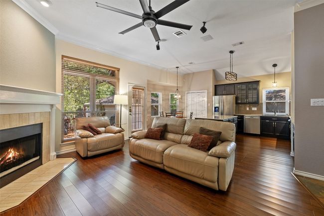 Living area with a tile fireplace, a ceiling fan, dark wood finished floors, crown molding, and baseboards | Image 9