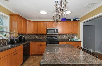 Kitchen featuring baseboard heating, a kitchen island, black dishwasher, and range with electric stovetop | Image 3