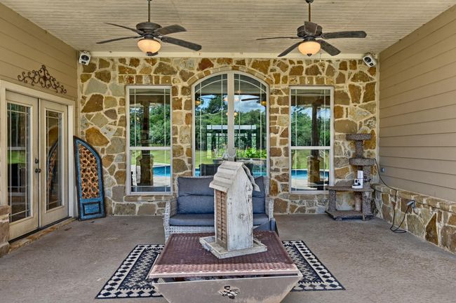 This inviting patio features rustic stone , two ceiling fans, and comfortable seating. It offers a view of the pool and spacious yard, perfect for relaxation and entertaining. | Image 36